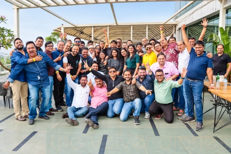 Corporate group photography showing a large group of former colleagues celebrating together at a professional reunion, with participants posing and raising their hands.