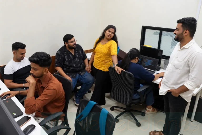Corporate workplace photography capturing employees collaborating and discussing work around computer stations in a professional office environment in Mumbai.